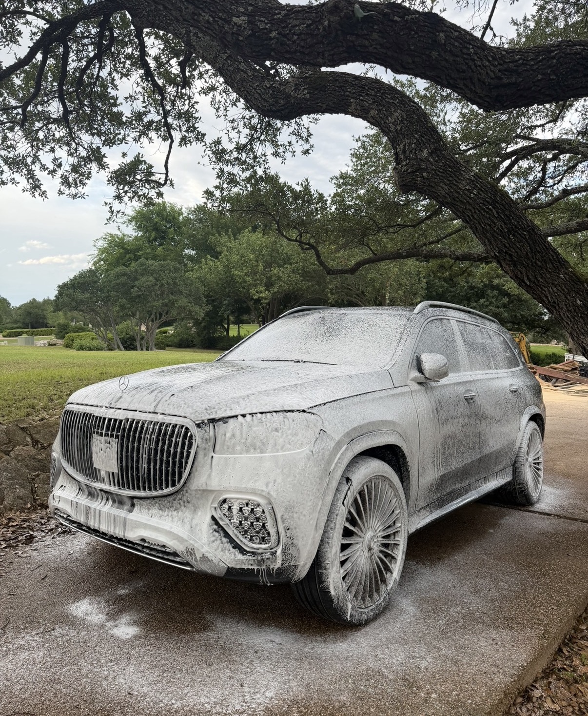 Luxury SUV covered in snow foam during a mobile detail in a driveway